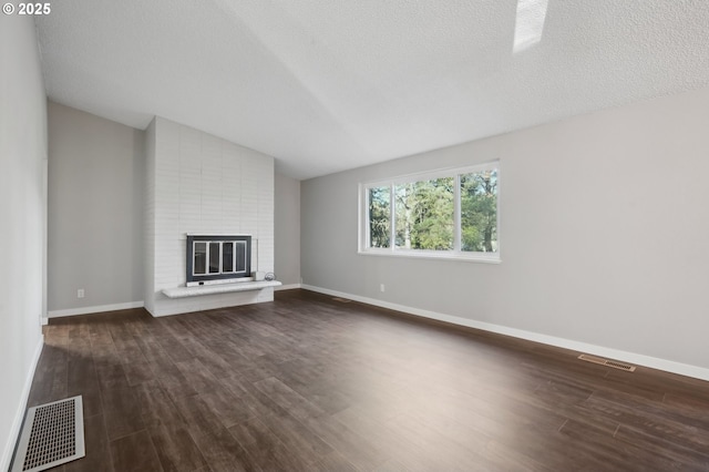 unfurnished living room featuring lofted ceiling, dark hardwood / wood-style floors, a textured ceiling, and a fireplace