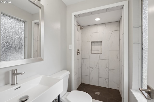 bathroom with a tile shower, sink, and toilet