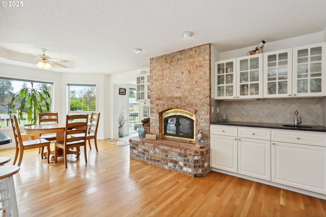 living room with a ceiling fan, a brick fireplace, light wood finished floors, and a textured ceiling