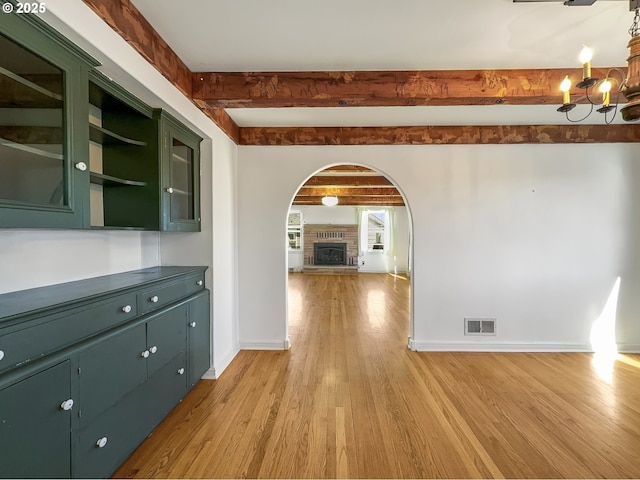 unfurnished dining area with light wood finished floors, baseboards, visible vents, and beamed ceiling