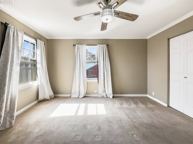 empty room featuring a wealth of natural light, carpet flooring, crown molding, and baseboards