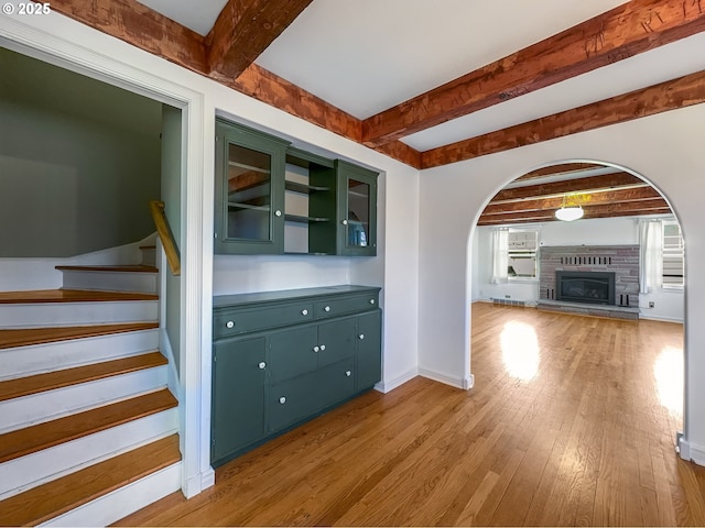 interior space with arched walkways, a glass covered fireplace, light wood-type flooring, baseboards, and stairs