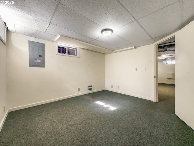 finished basement featuring visible vents, baseboards, electric panel, a drop ceiling, and dark carpet