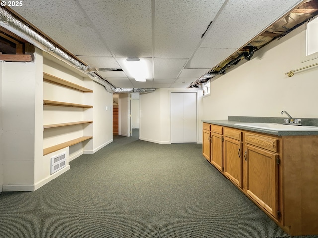 finished basement with dark carpet, a paneled ceiling, a sink, and baseboards