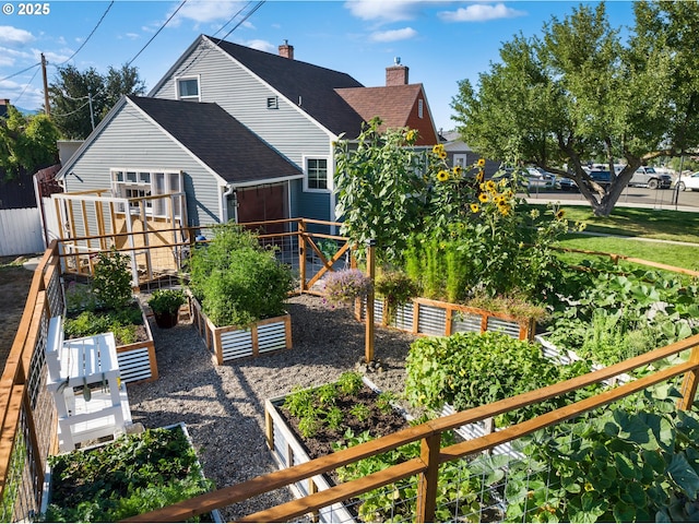 exterior space featuring a shingled roof, fence, a vegetable garden, and a chimney