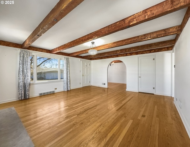 unfurnished living room featuring arched walkways, wood finished floors, visible vents, baseboards, and beam ceiling