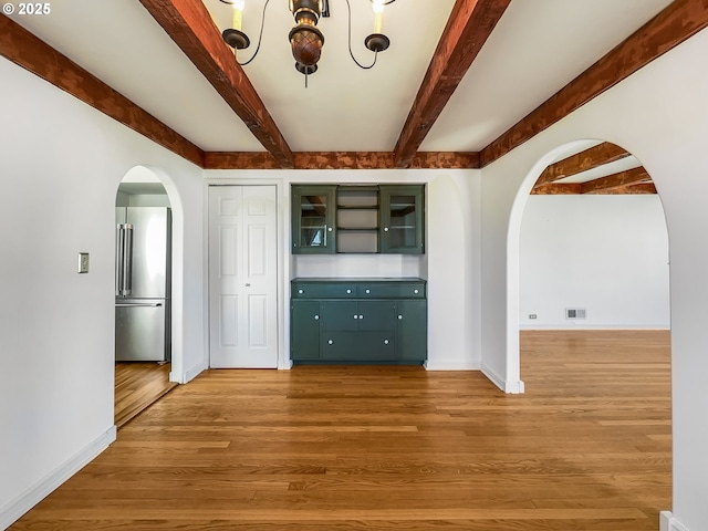 empty room featuring arched walkways, visible vents, light wood-type flooring, beamed ceiling, and baseboards