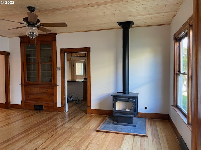 unfurnished living room with light wood finished floors, baseboards, wood ceiling, a wood stove, and crown molding