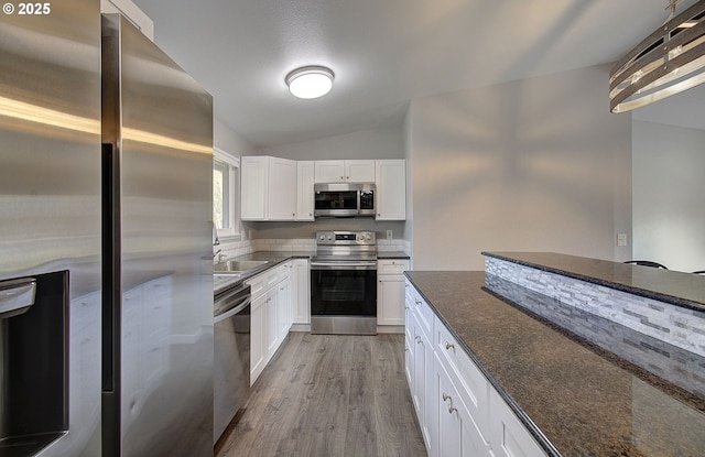 kitchen with lofted ceiling, dark stone countertops, light wood-type flooring, appliances with stainless steel finishes, and white cabinets