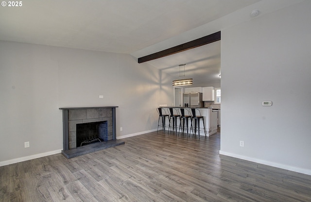 unfurnished living room featuring hardwood / wood-style flooring, a tiled fireplace, and vaulted ceiling with beams