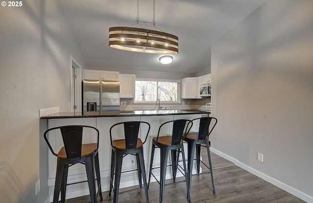 kitchen with a breakfast bar, sink, white cabinets, kitchen peninsula, and stainless steel appliances