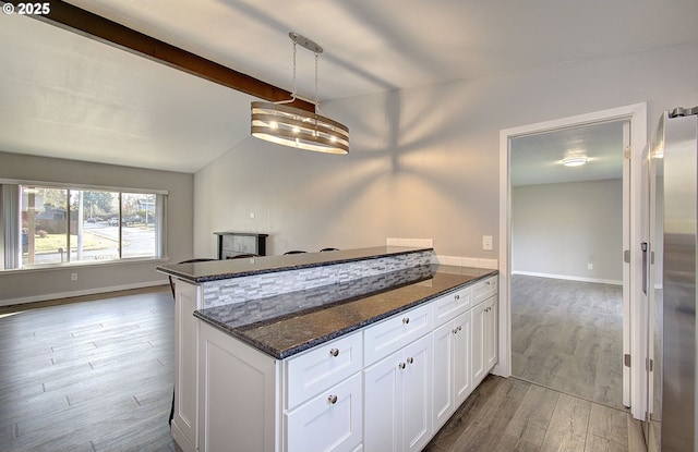 kitchen featuring white cabinetry, decorative light fixtures, stainless steel fridge, hardwood / wood-style flooring, and dark stone counters