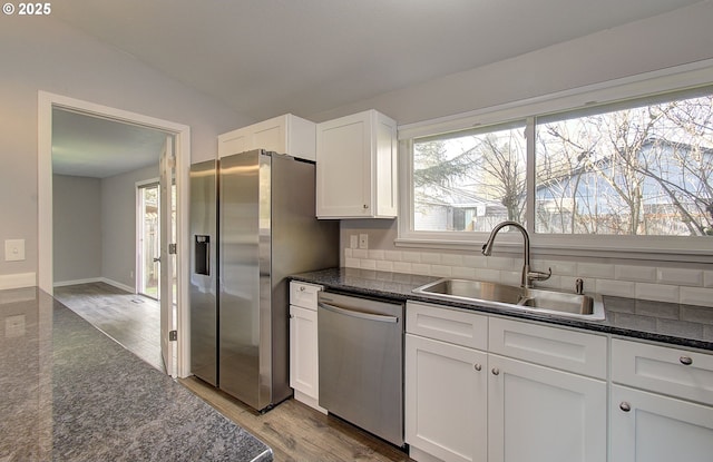 kitchen featuring appliances with stainless steel finishes, white cabinetry, sink, dark stone countertops, and a healthy amount of sunlight