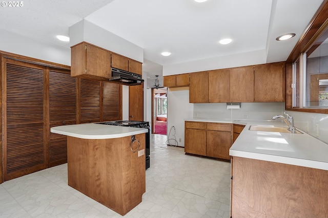 kitchen featuring a sink, black gas range, brown cabinetry, light countertops, and under cabinet range hood