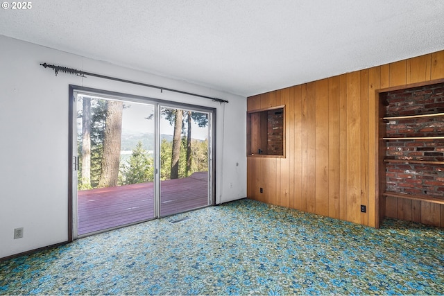 carpeted empty room featuring wooden walls, a textured ceiling, and visible vents