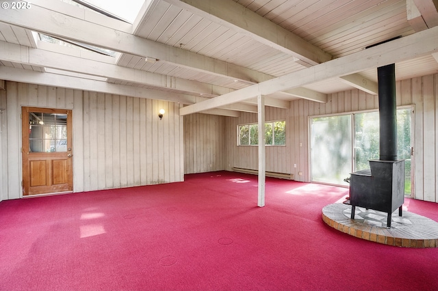 basement featuring a baseboard heating unit, carpet, a wood stove, and wood walls