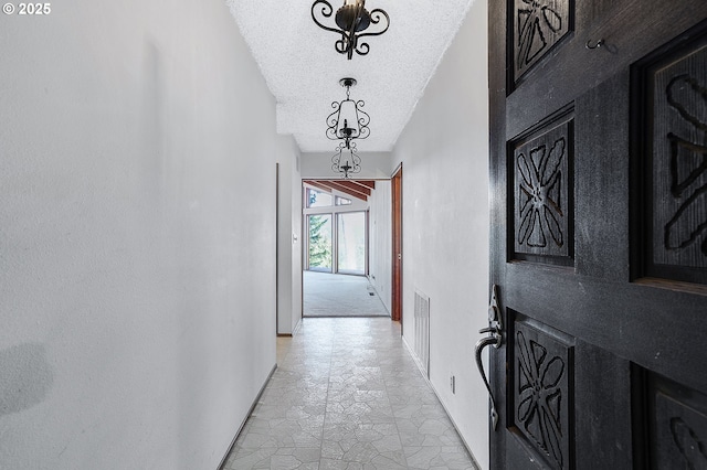 hallway featuring a textured ceiling, baseboards, a notable chandelier, stone finish floor, and visible vents