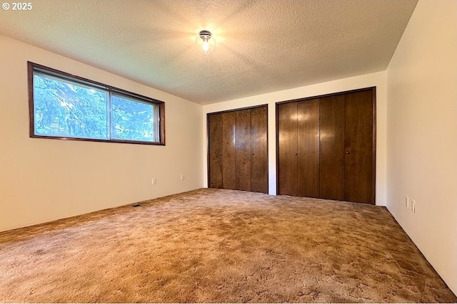 unfurnished bedroom with multiple closets, carpet, and a textured ceiling