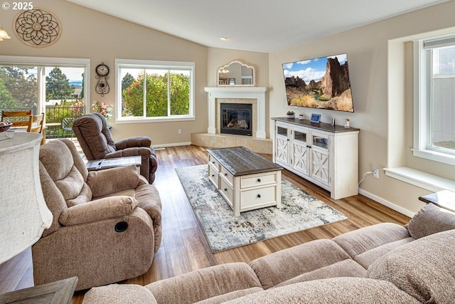 living room with a tiled fireplace, vaulted ceiling, and light hardwood / wood-style floors