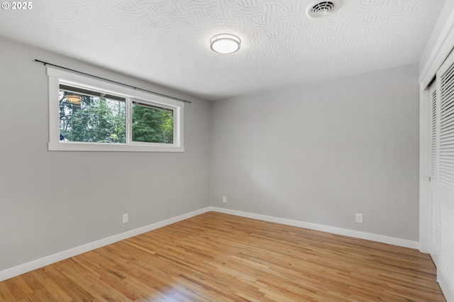unfurnished bedroom featuring a textured ceiling, visible vents, baseboards, a closet, and light wood-style flooring