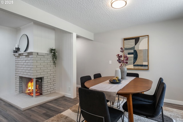 dining space with baseboards, a textured ceiling, wood finished floors, and a fireplace