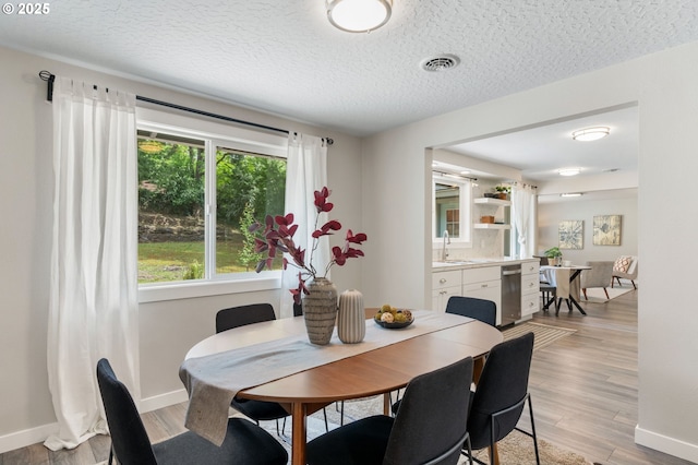 dining area with a textured ceiling, visible vents, baseboards, and light wood-type flooring
