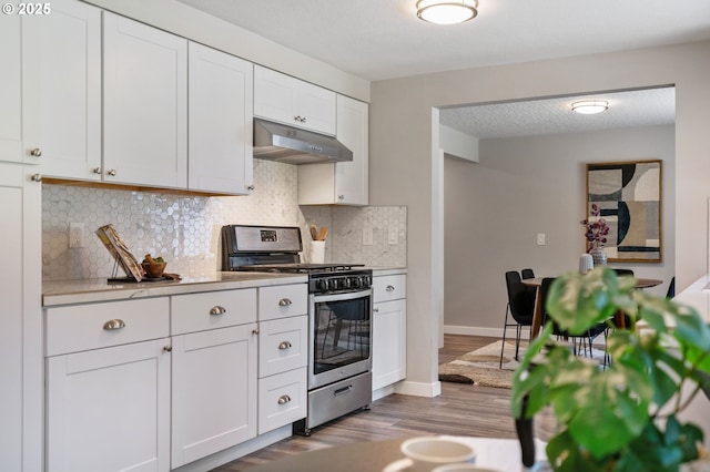 kitchen with stainless steel gas stove, light countertops, decorative backsplash, wood finished floors, and under cabinet range hood