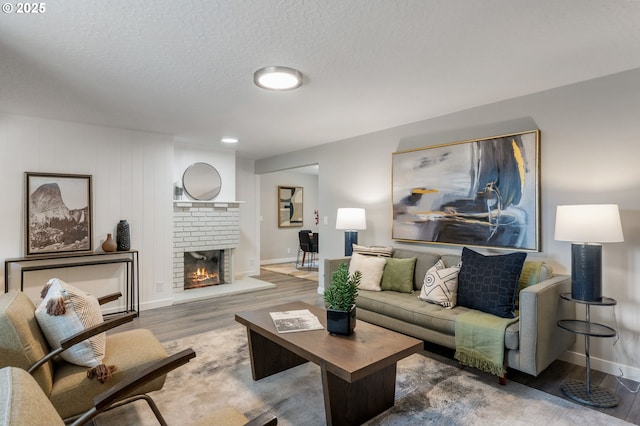 living room with a textured ceiling, baseboards, a brick fireplace, and wood finished floors