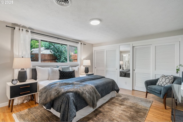 bedroom featuring multiple closets, light wood-type flooring, a textured ceiling, and visible vents