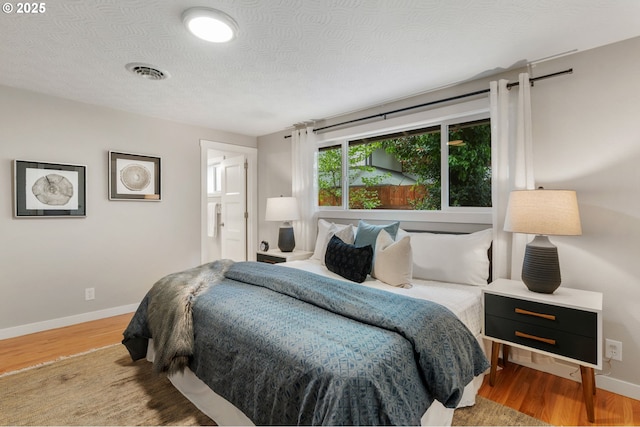 bedroom with connected bathroom, a textured ceiling, baseboards, wood finished floors, and visible vents