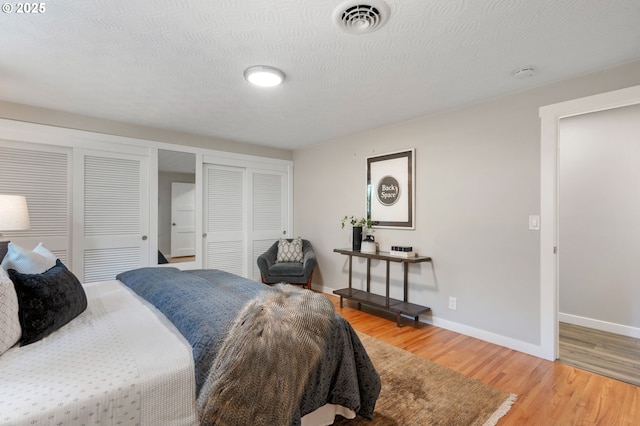 bedroom featuring multiple closets, baseboards, light wood-type flooring, and visible vents