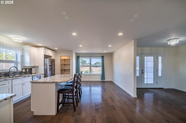 kitchen with a sink, stainless steel fridge, white cabinetry, dark wood-style flooring, and light stone countertops