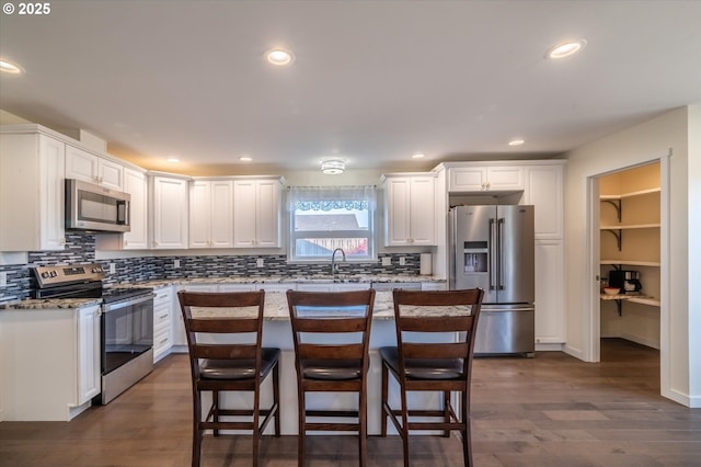 kitchen with white cabinets, a kitchen breakfast bar, backsplash, dark wood-type flooring, and appliances with stainless steel finishes