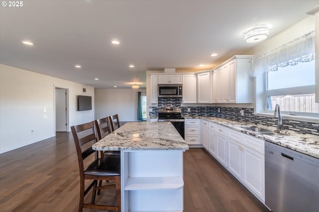 kitchen featuring white cabinets, stainless steel appliances, backsplash, a sink, and a breakfast bar area