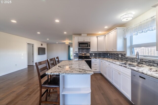 937 Carter St SW, Bandon, OR 97411 - kitchen featuring appliances with stainless steel finishes, a sink, backsplash, white cabinets, and a breakfast bar area