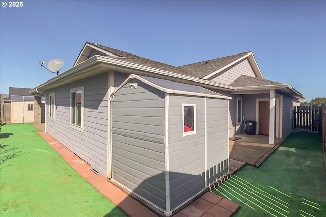 view of side of property with fence, an outdoor structure, roof with shingles, and a storage shed