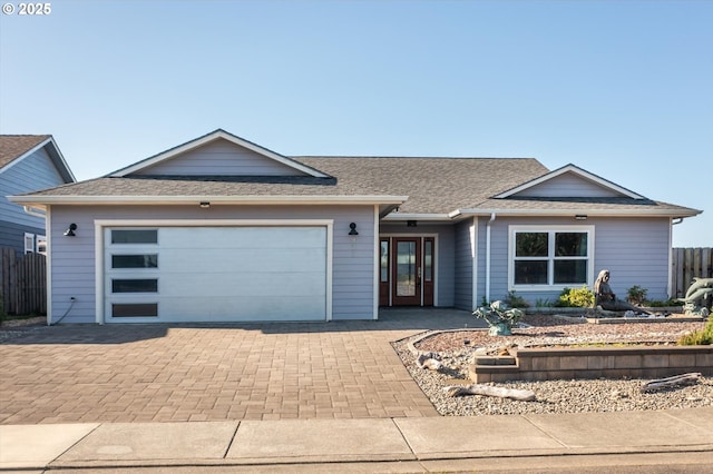 view of front of property featuring roof with shingles, decorative driveway, fence, and a garage