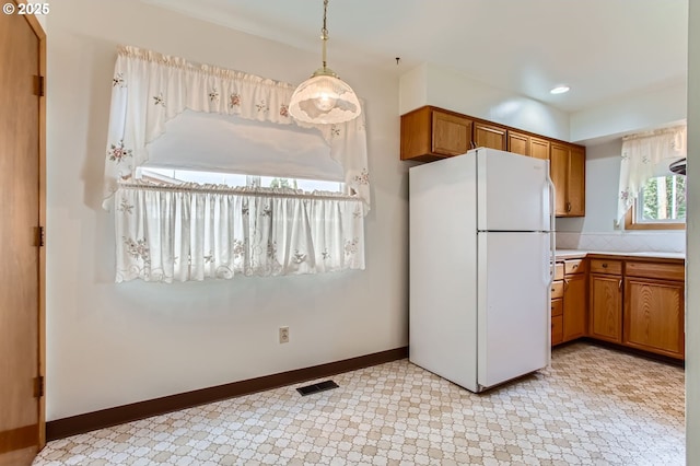 kitchen featuring brown cabinetry, freestanding refrigerator, light countertops, and visible vents