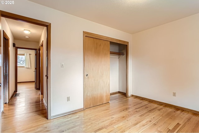 unfurnished bedroom featuring a closet, visible vents, light wood-style flooring, and baseboards