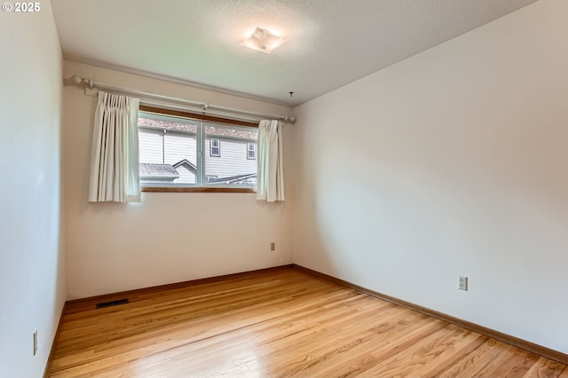 unfurnished room with light wood-style flooring, visible vents, and baseboards