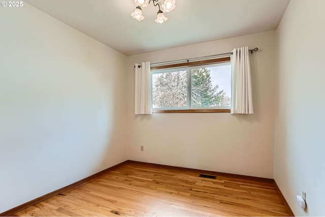 spare room with light wood-style floors, visible vents, a notable chandelier, and baseboards