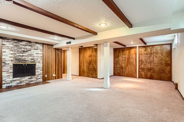 finished basement featuring a textured ceiling, wood walls, carpet flooring, visible vents, and a brick fireplace