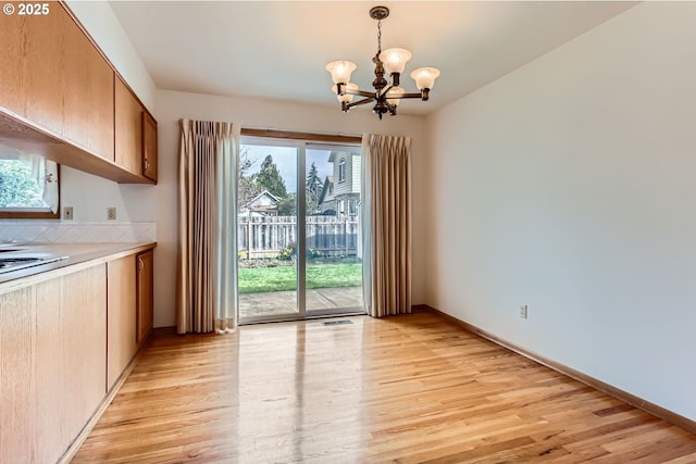 unfurnished dining area featuring baseboards, light wood finished floors, visible vents, and a notable chandelier