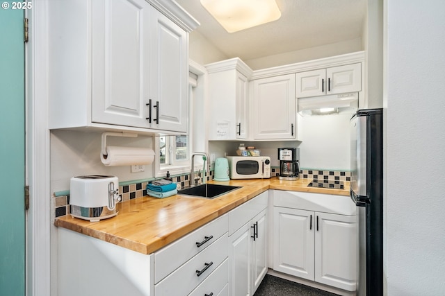 kitchen featuring white cabinets, wooden counters, sink, backsplash, and stainless steel fridge