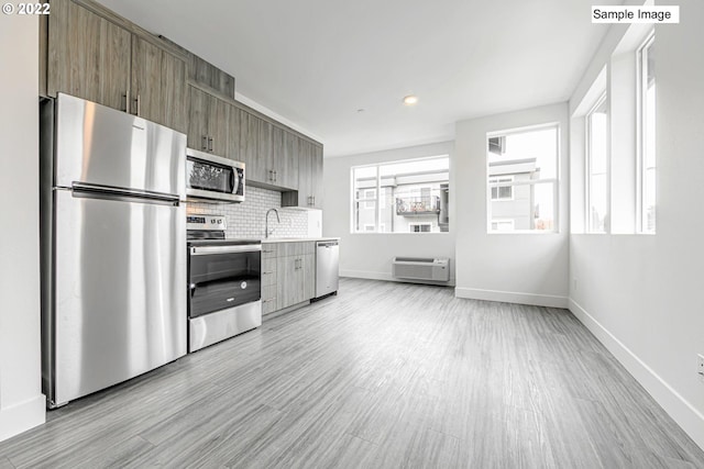 kitchen with appliances with stainless steel finishes, sink, backsplash, and light wood-type flooring