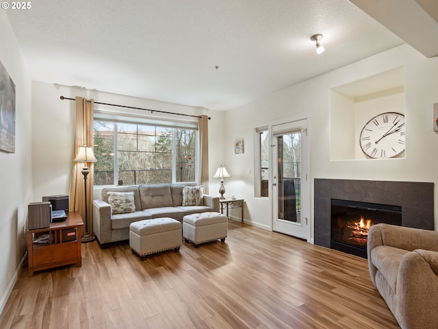635 NW Lost Springs Ter Unit 104, Portland, OR 97229 - living room featuring wood finished floors, a tiled fireplace, baseboards, and plenty of natural light
