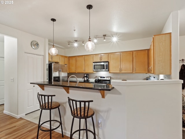kitchen with decorative light fixtures, a peninsula, light wood-style floors, stainless steel appliances, and a breakfast bar area