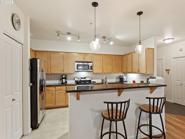 635 NW Lost Springs Ter Unit 104, Portland, OR 97229 - kitchen with appliances with stainless steel finishes, a kitchen breakfast bar, light brown cabinets, a sink, and hanging light fixtures
