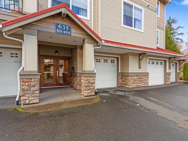 entrance to property featuring metal roof, stone siding, an attached garage, french doors, and driveway