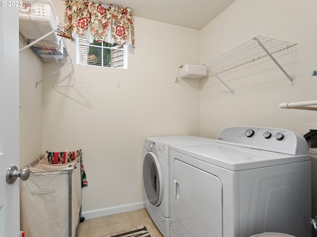 clothes washing area with light tile patterned floors, washing machine and clothes dryer, laundry area, and baseboards